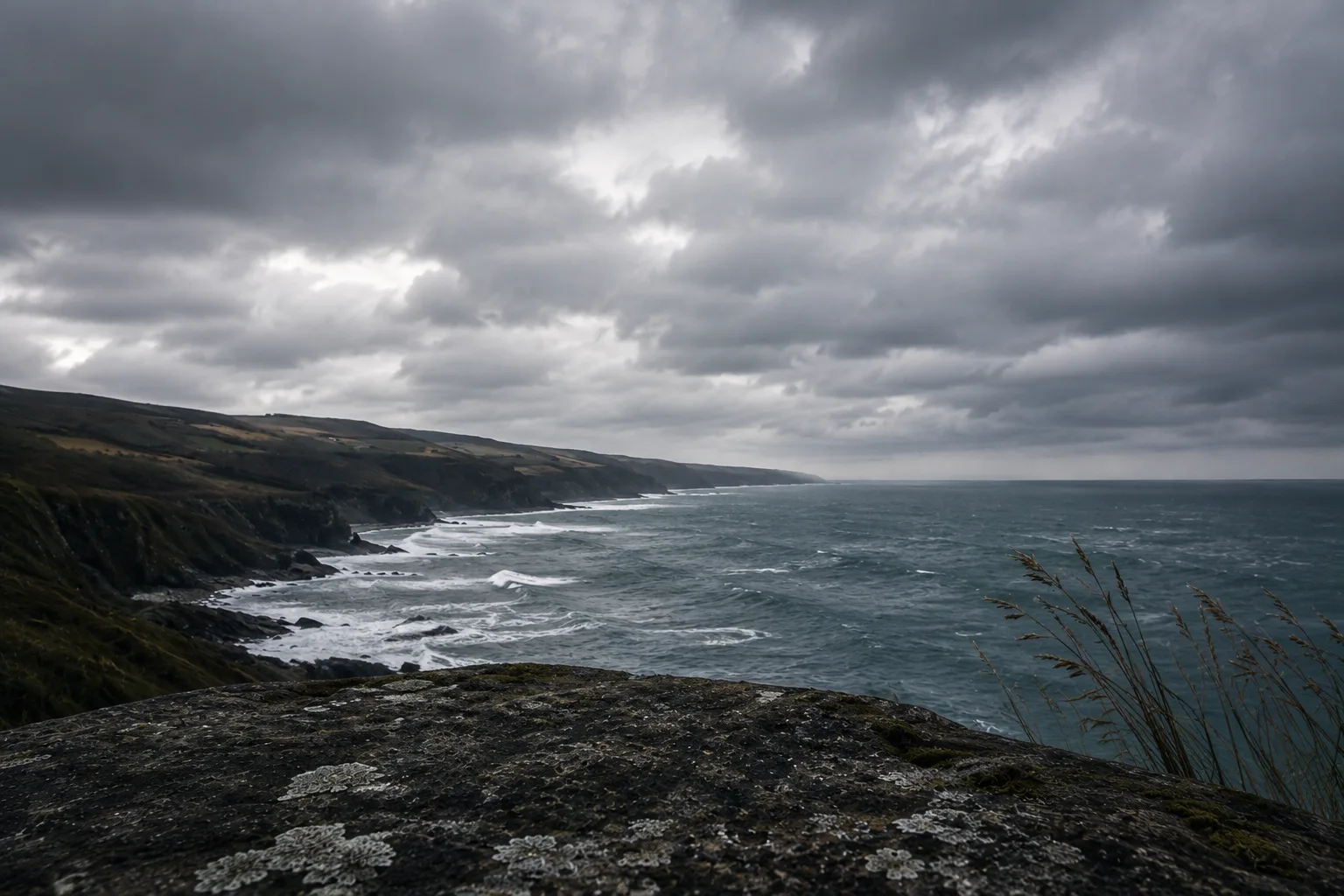 A dramatic stormy coastline with cliffs and crashing waves, viewed from a mossy rock outcrop